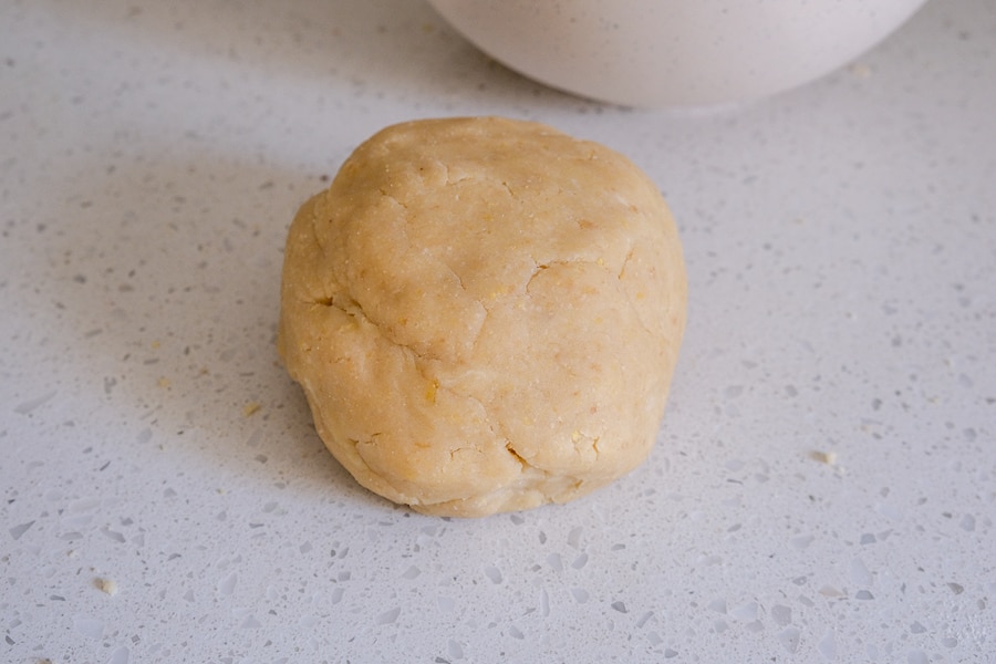 ball of cookie dough sitting on white counter top with bowl behind