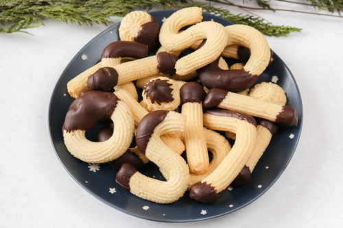 german spritz cookies on blue plate on counter top with green branch behind