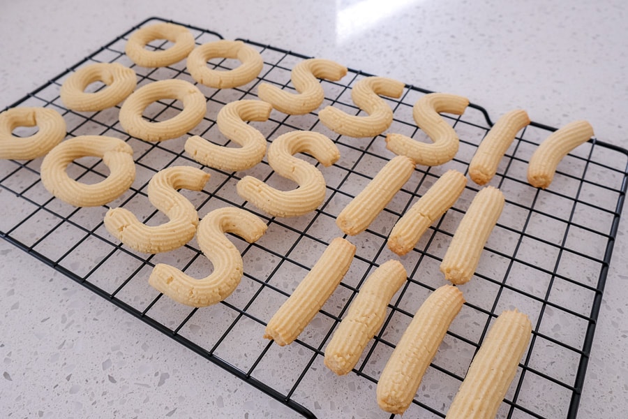 cooked spritz cookies on cooling rack on white counter top