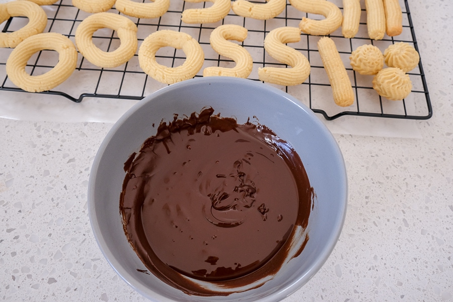 bowl of melted chocolate with cookies on cooling rack behind