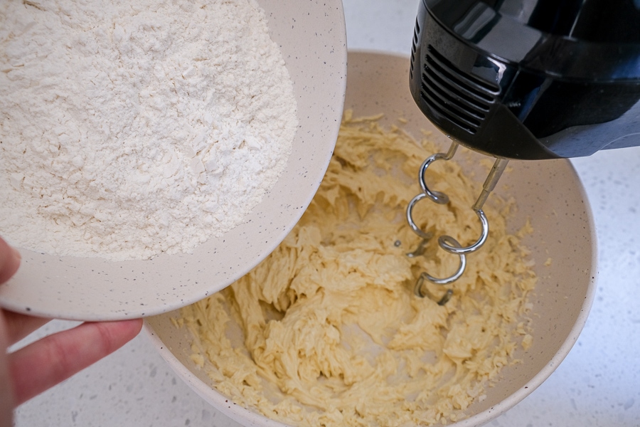 pouring dry ingredients from bowl into cookie dough with beaters in bowl