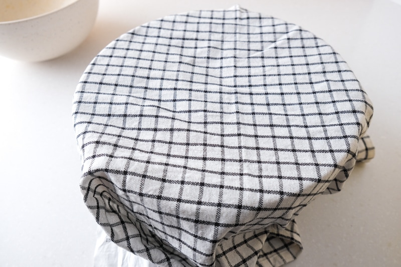 checkered dish towel covering mixing bowl sitting on white counter.