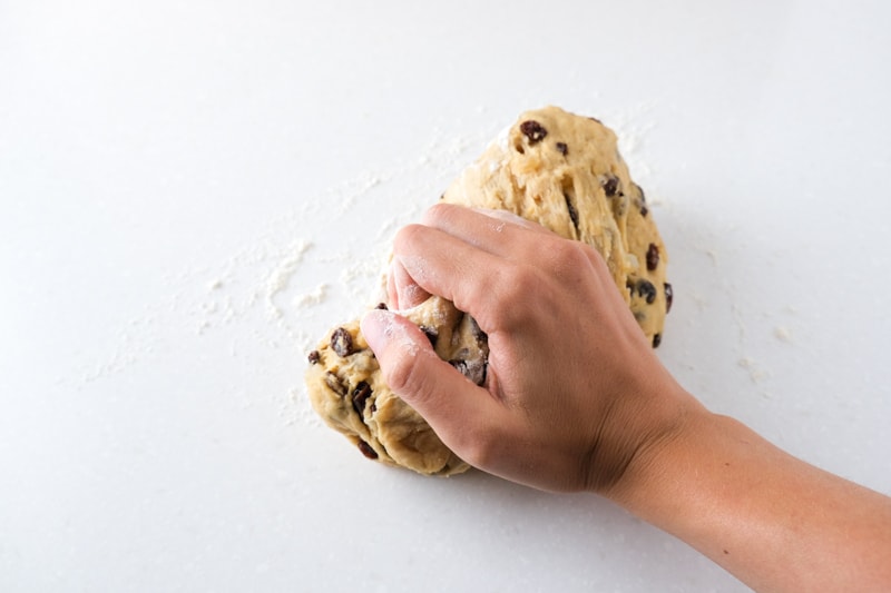hand kneading ball of stollen dough on white countertop.