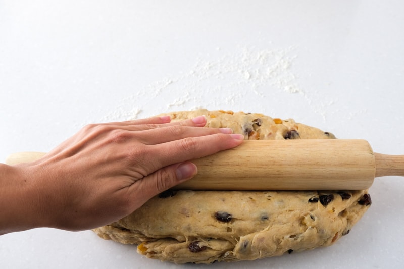 hand pressing wooden rolling pin into stollen dough lengthwise on countertop.