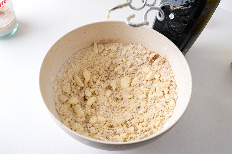 chunky bread dough in white mixing bowl with black hand mixer beside.