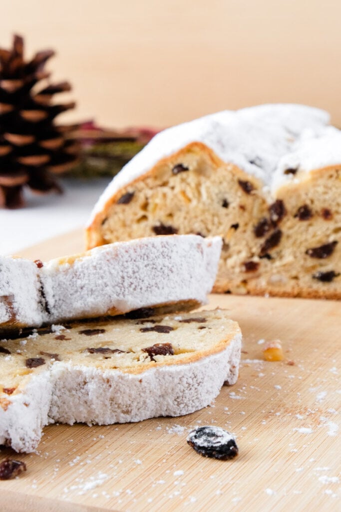 german christmas bread with raisins on wooden board with two slices cut in front and pine cone behind.