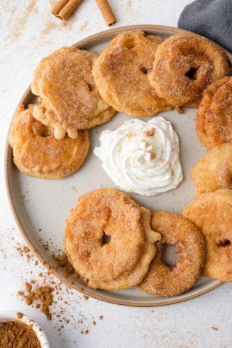 round plate of german fried apple rings covered in sugar with whipped cream in the center of plate.