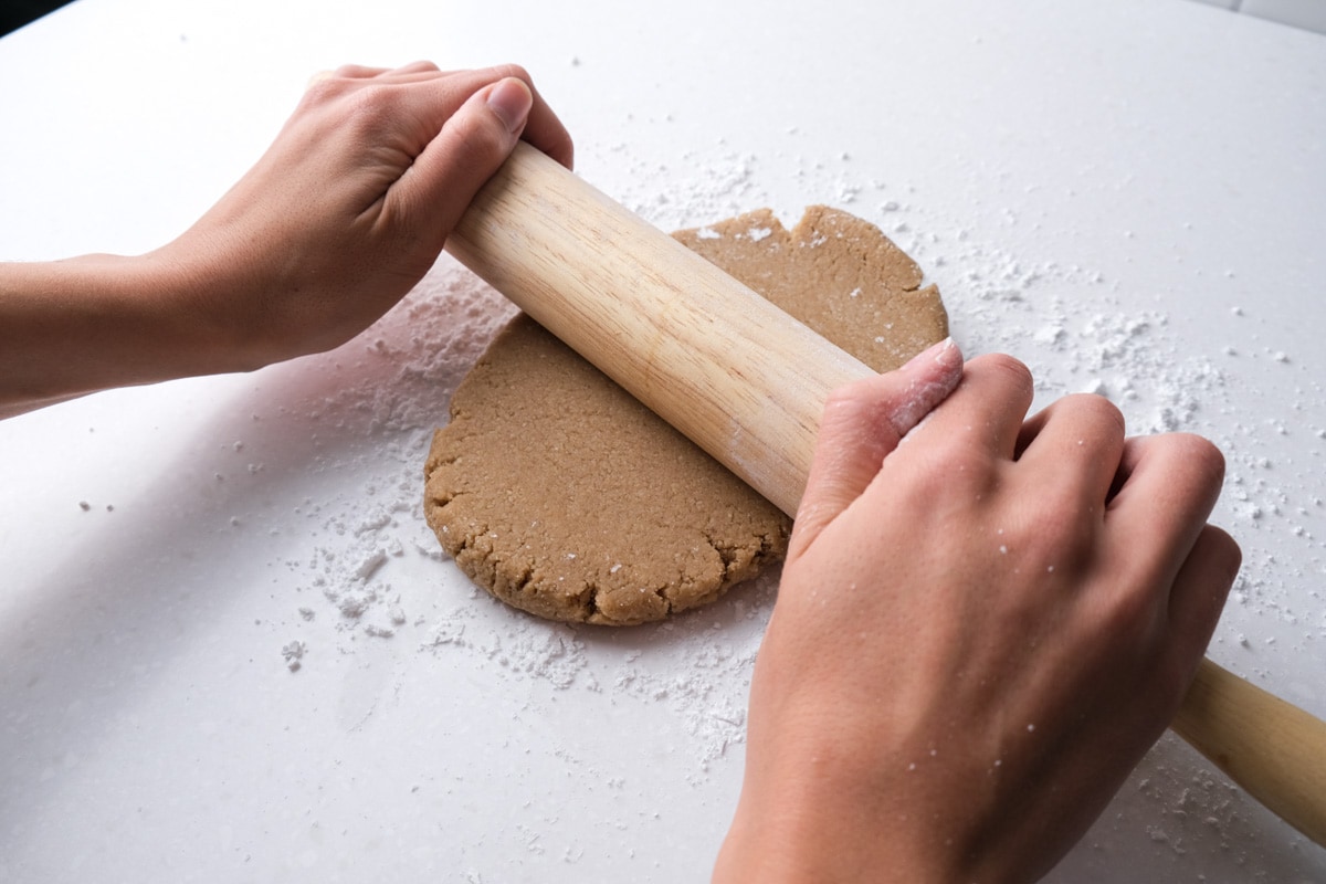 hand holding wooden rolling pin rolling ball of dough out on white counter top.