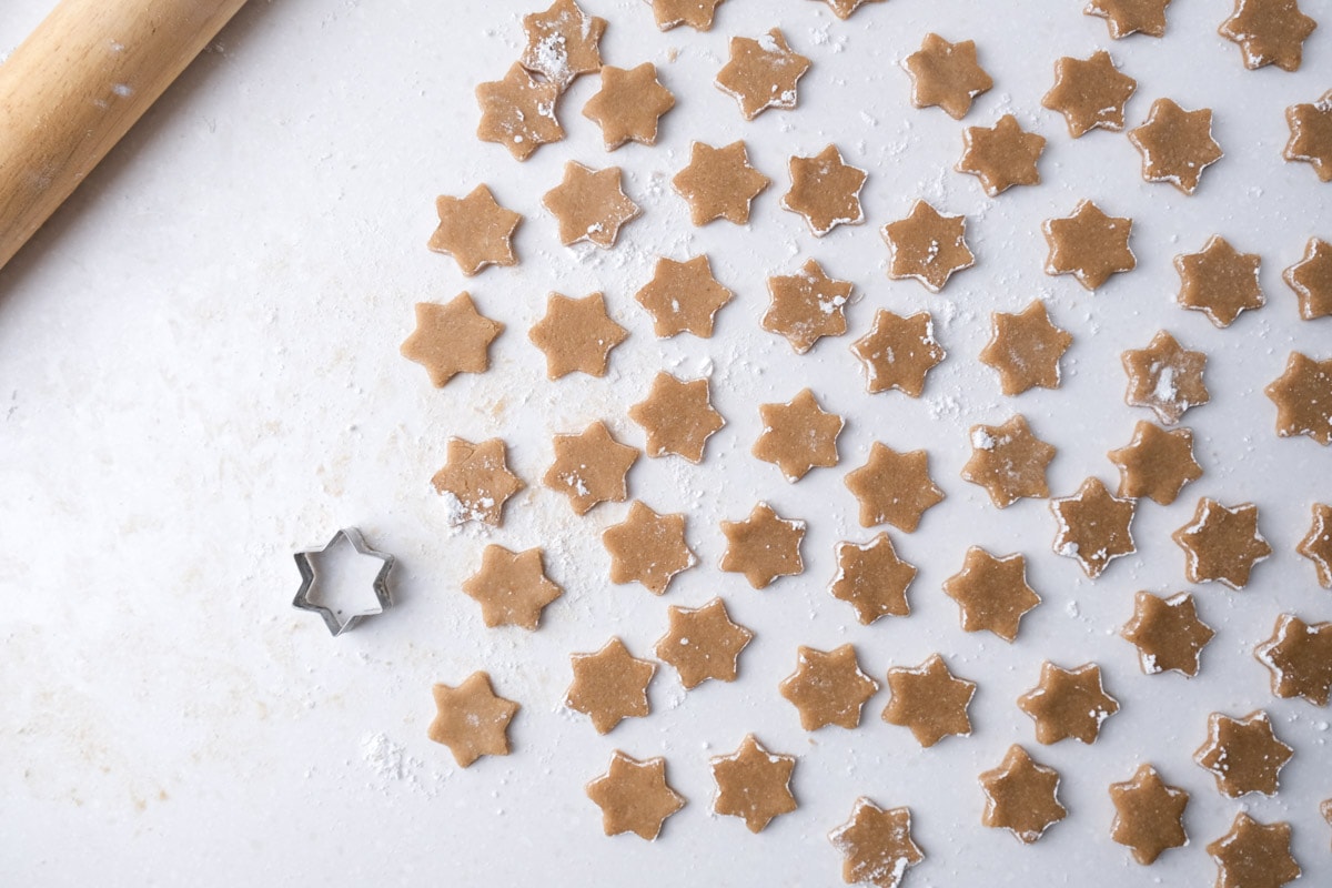 many raw cinnamon star cookies sitting on white counter with cookie cutter beside.