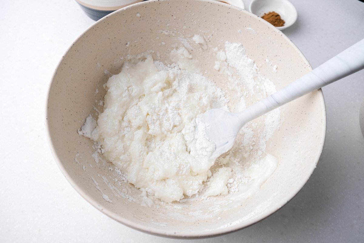 white spatula folding powdered sugar into egg whites in white mixing bowl.