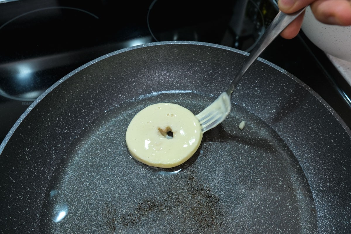 battered apple ring sitting in frying oil in pan with silver fork beside.