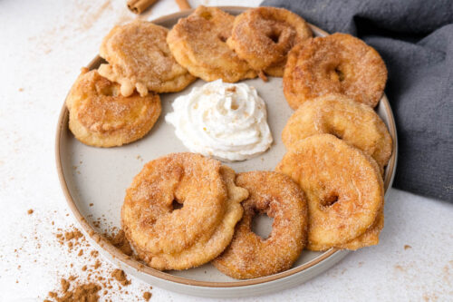 plate of fried german apple rings with whipping cream in the center on white counter.