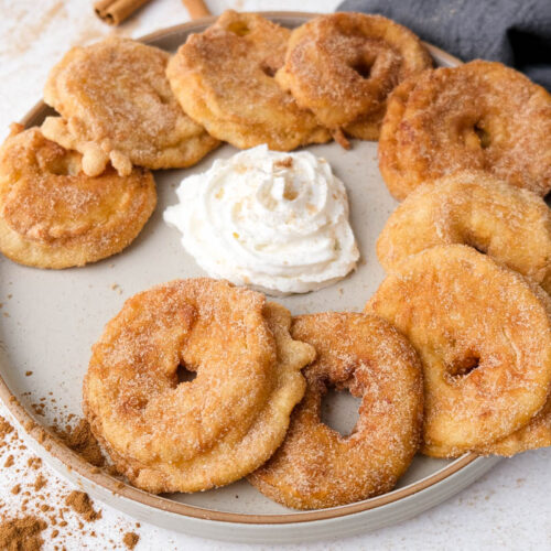 plate of fried german apple rings with whipping cream in the center on white counter.