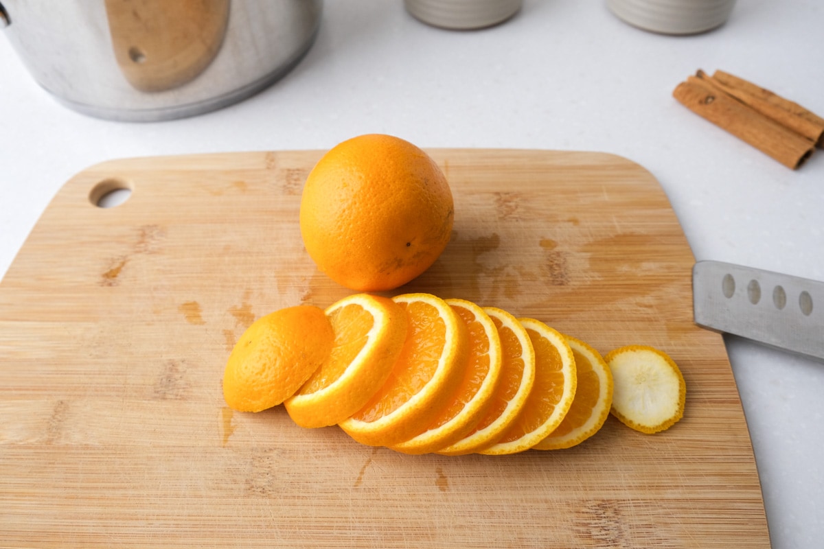 orange cut into slices on wooden cutting board with knife beside and whole orange behind.