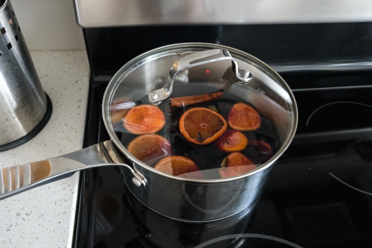 silver pot of german mulled wine on black stovetop.