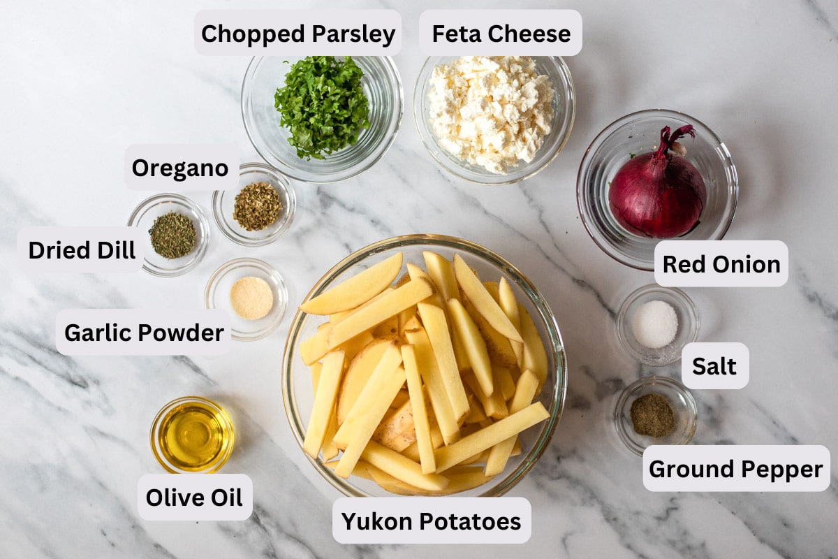 ingredients for greek fries in bowls on counter with labels seen from above.