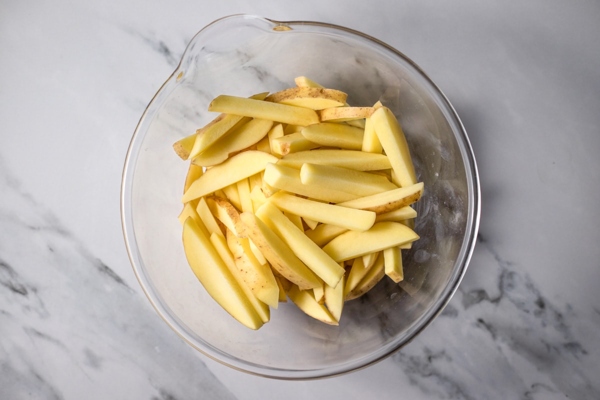 raw french fries sitting in glass bowl on counter top.