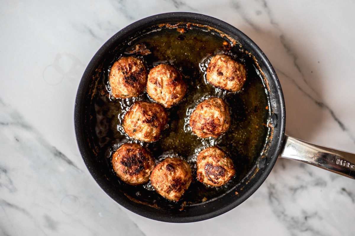greek meatballs frying in cast iron pan filled with oil sitting on counter top.