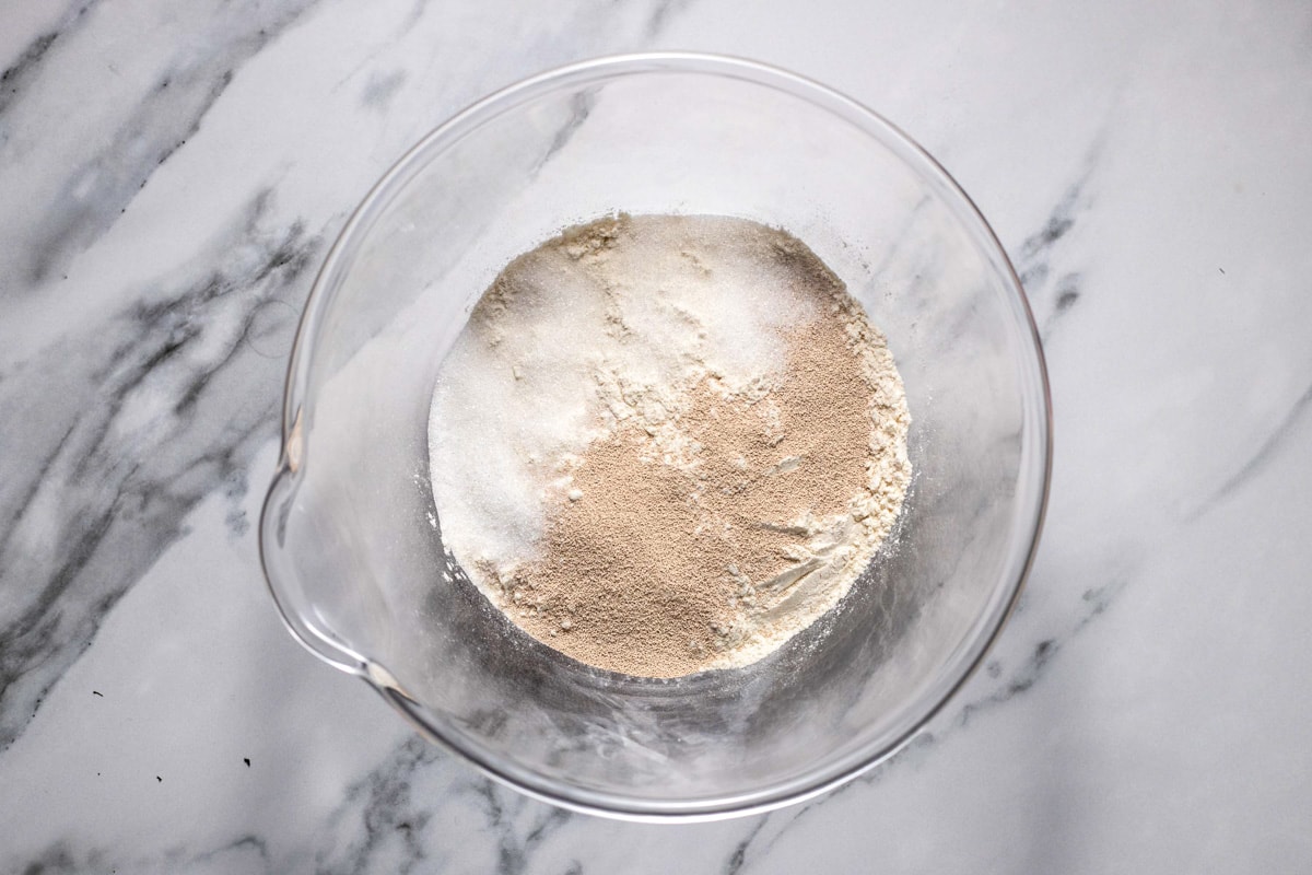 dry yeast and flour in a clear glass mixing bowl on counter top.