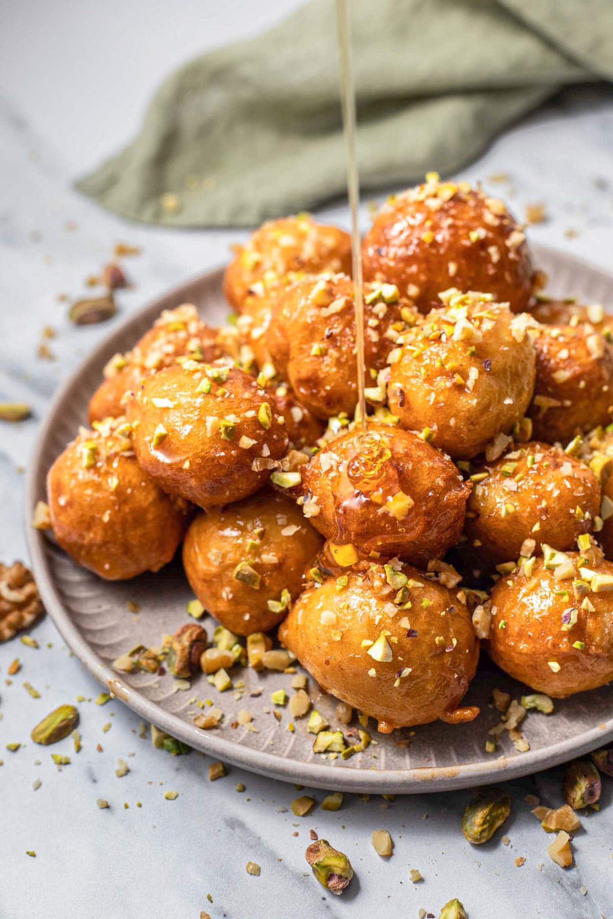 greek honey balls covered in nuts with drizzling honey on top. 