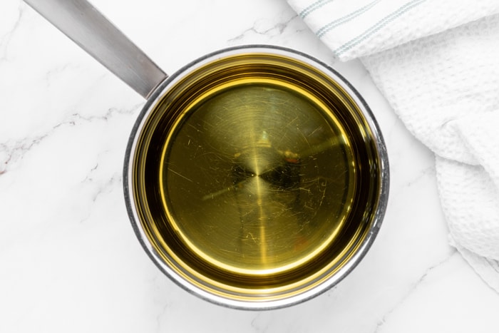 silver pot with cooking oil sitting on white marble counter.