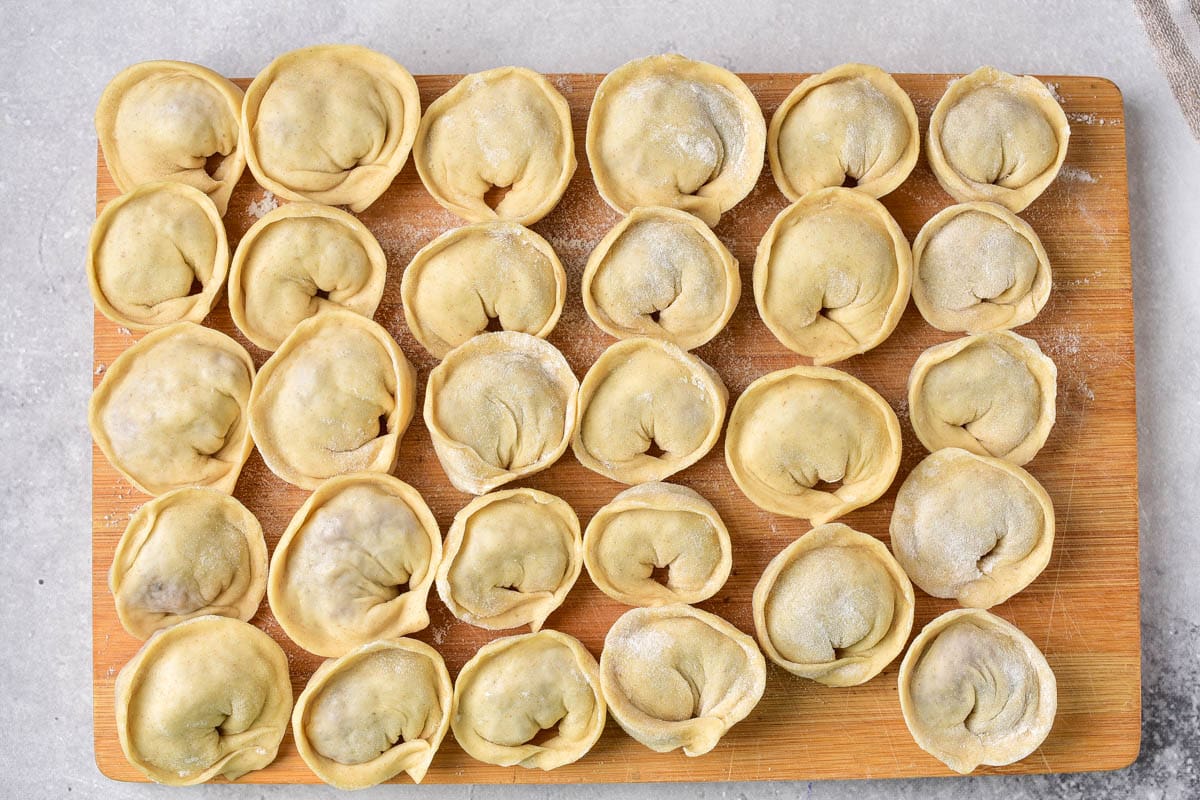 freshly folded pelmeni dumplings sitting in rows on wooden cutting board.