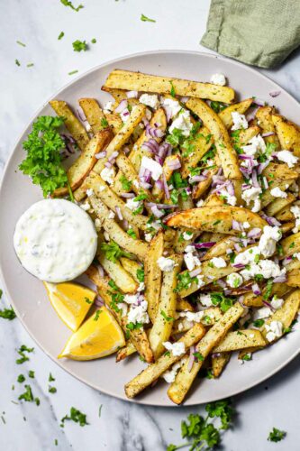 plate with fries covered in feta parsley and onions on grey counter top.