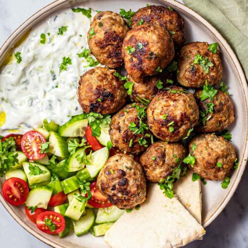 greek meatballs on plate with tzatziki and salad.