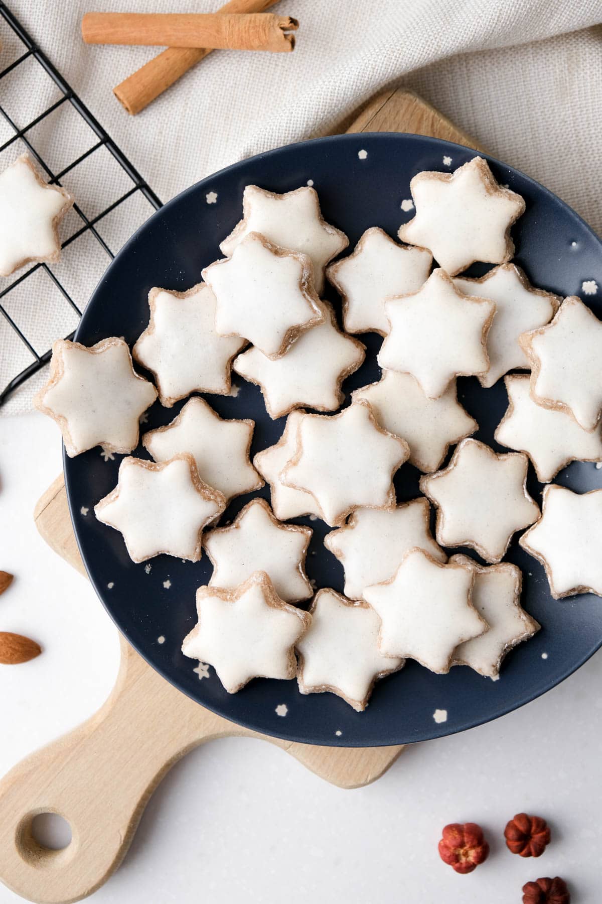 cinnamon star cookies with icing on blue plate sitting on wooden board with cookies and almonds around.