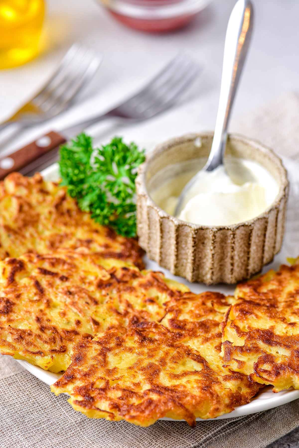 potato pancakes laying flat on plate with dish of sour cream and spoon behind beside parsley.