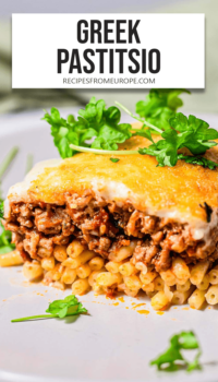 slice of pastitio on white plate with parsley on top and text overlay "Greek Pastitsio".