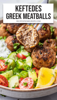 meatball on fork with bite taken out and more meatballs, salad, and tzatziki on plate in background plus text overlay "Keftedes Greek Meatballs".