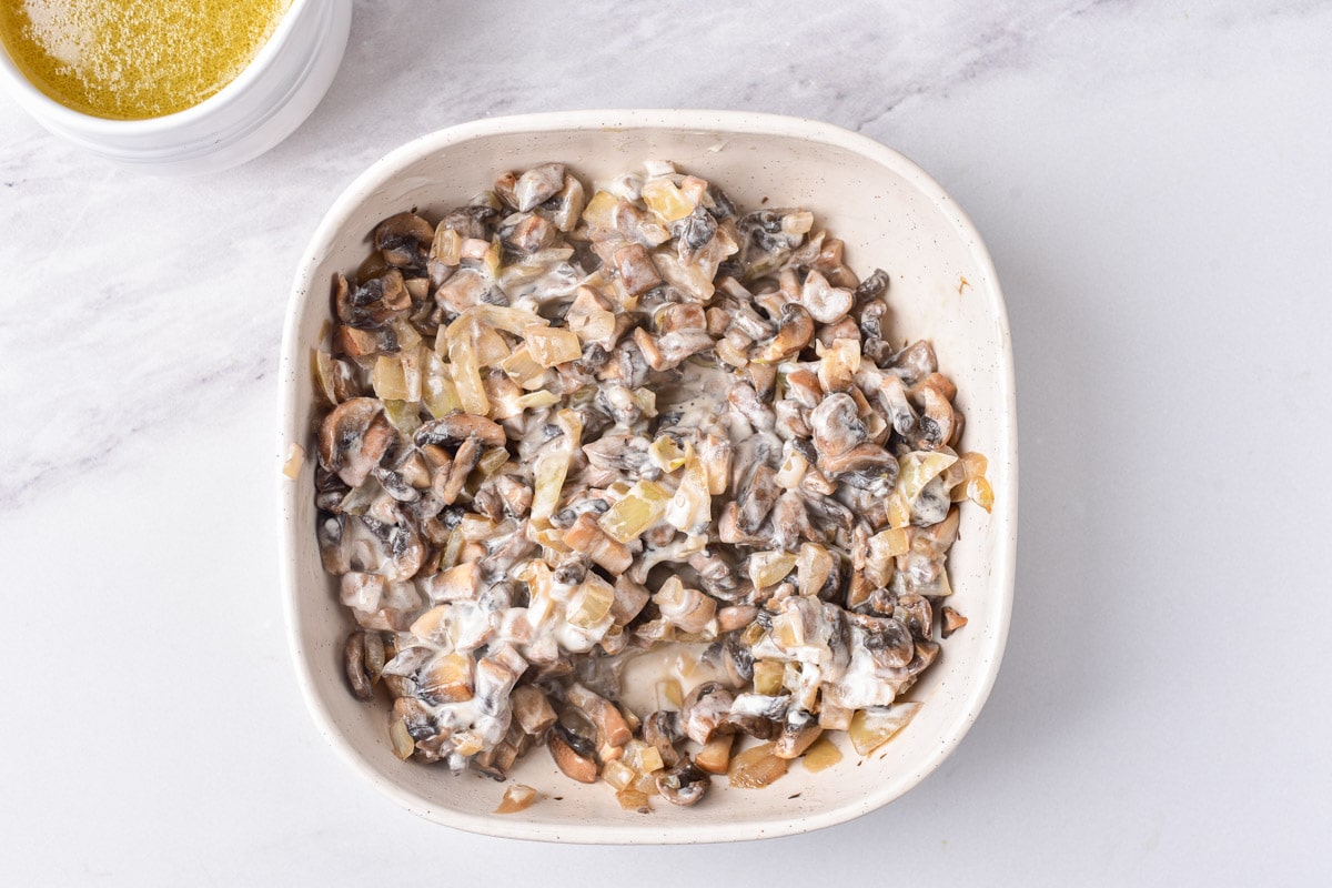 cooked mushrooms and onions in sour cream in a white pan on counter top.