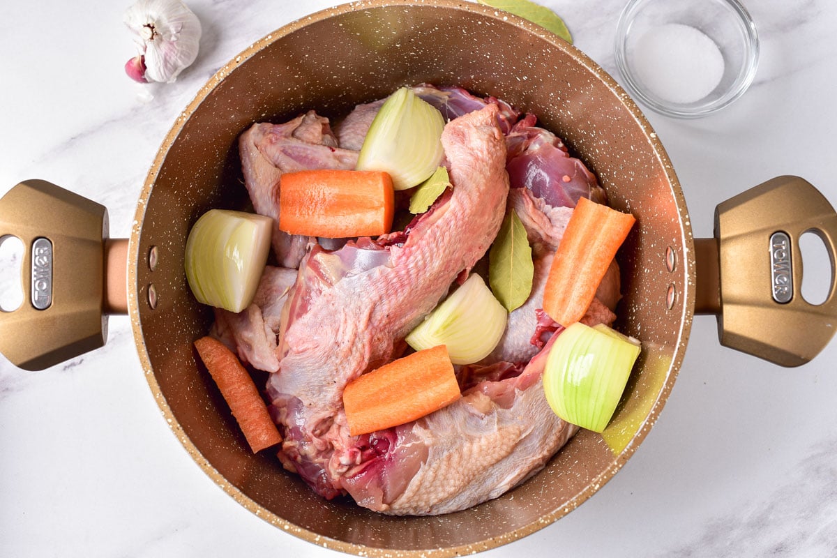 raw chicken in pot with raw carrots and onions.
