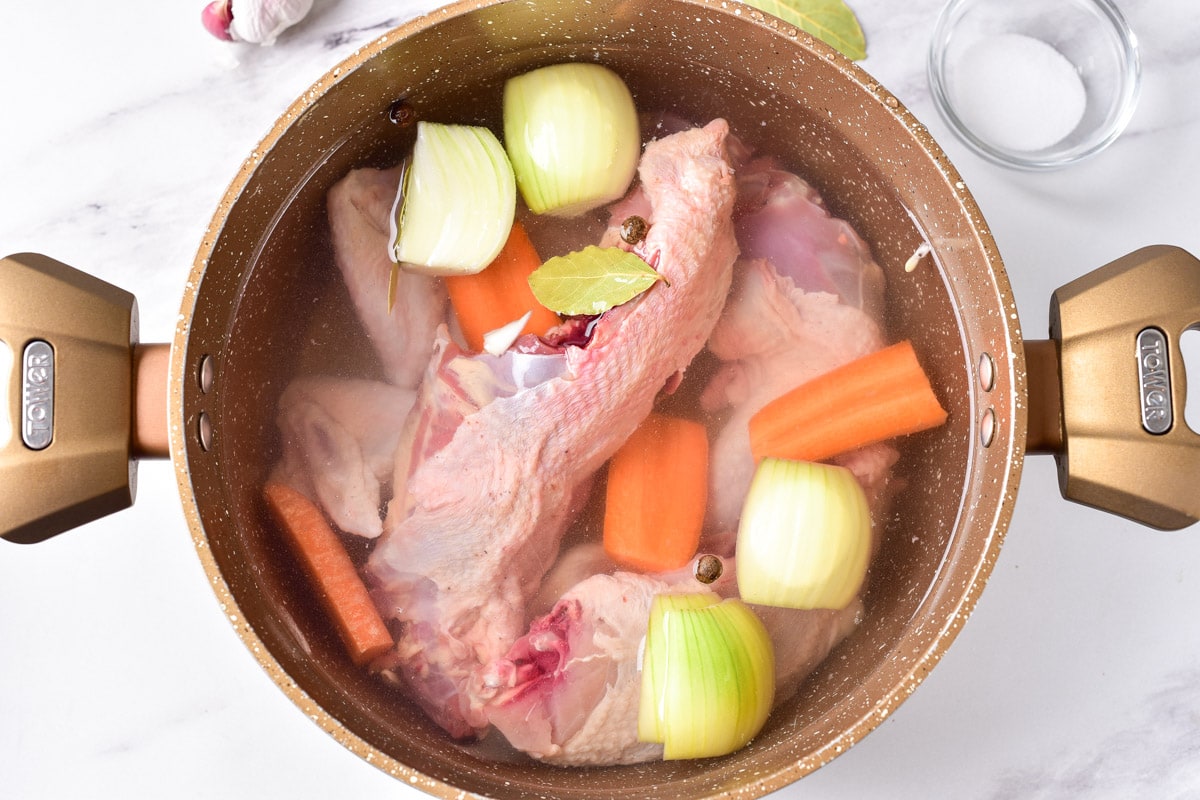 raw chicken and onions and carrots in large pot filled with water on counter top.