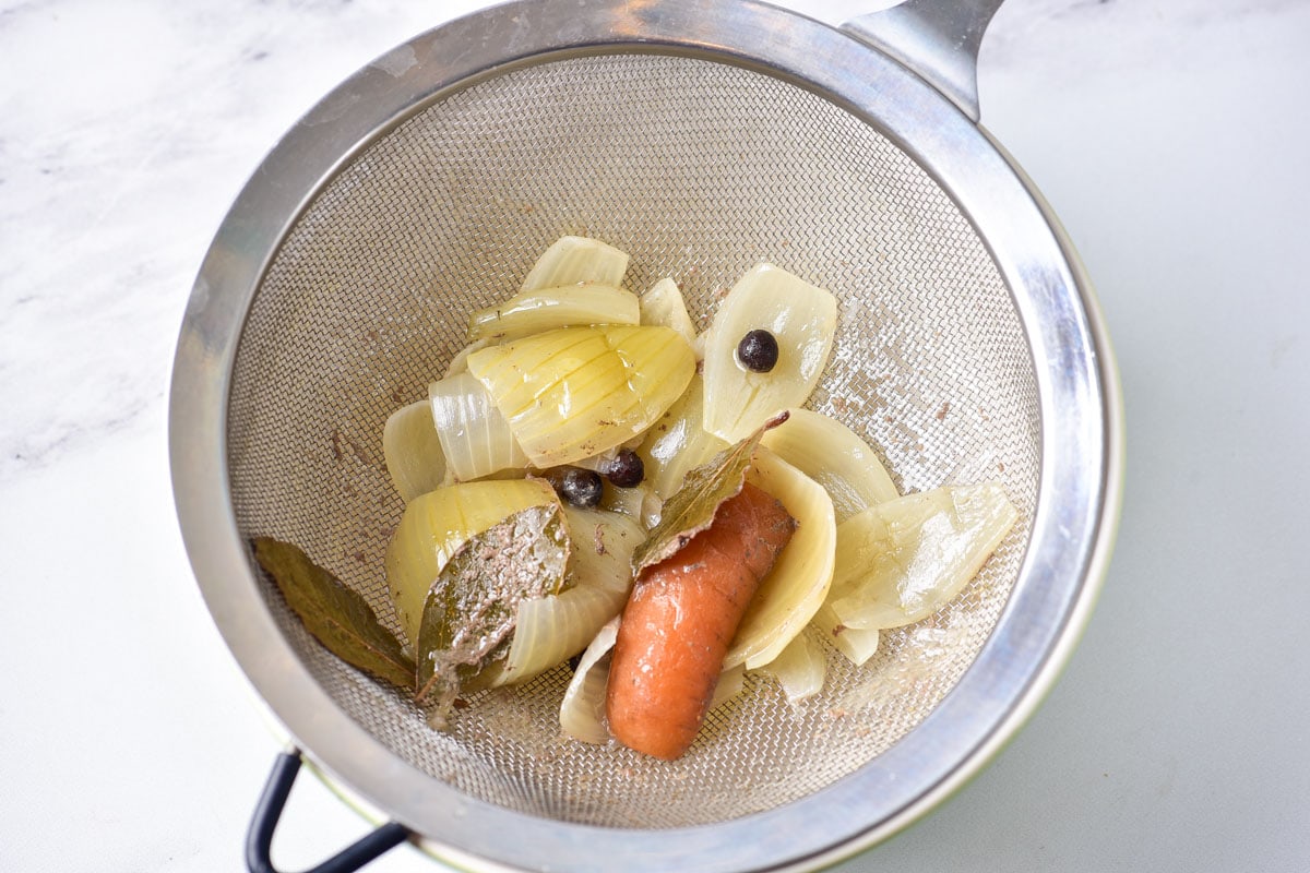 cooked onion and vegetables and spices in metal strainer over top of a bowl sitting on the counter.