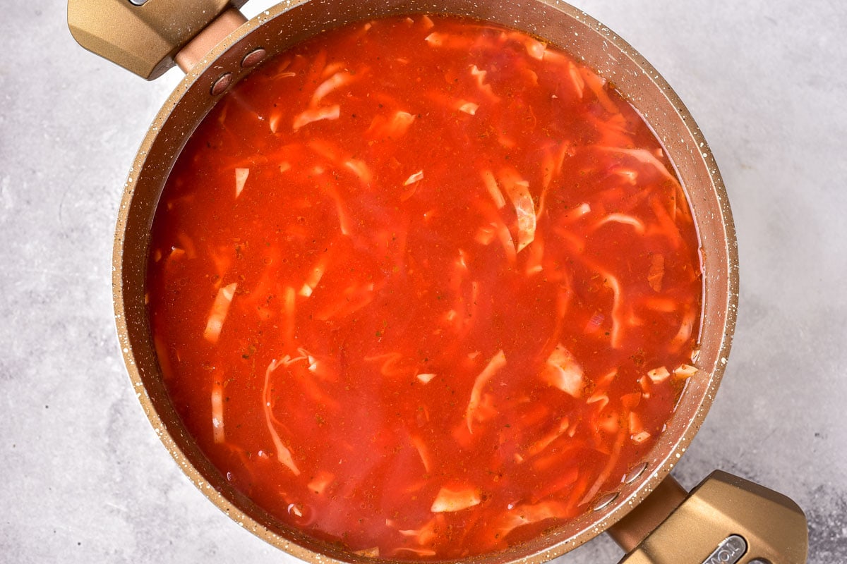 red broth in large pot sitting on grey counter top.