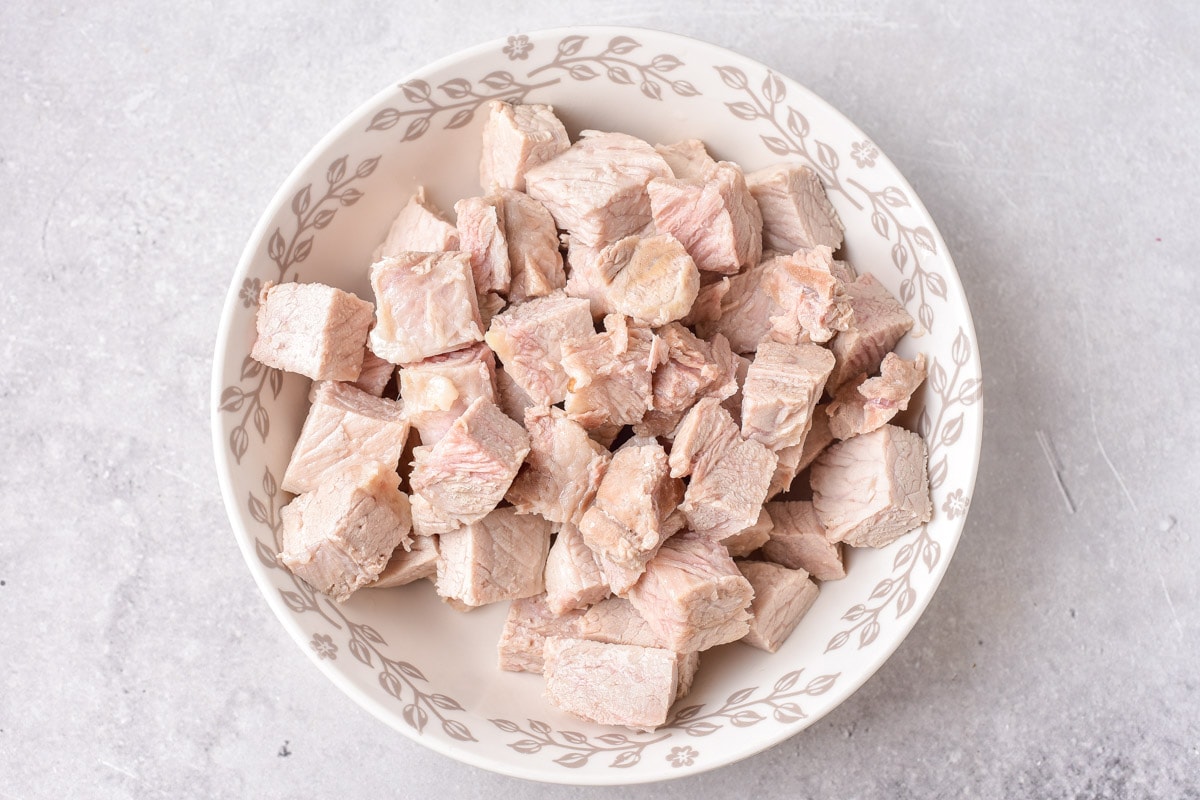 chunks of cooked pork on white plate on grey counter top.