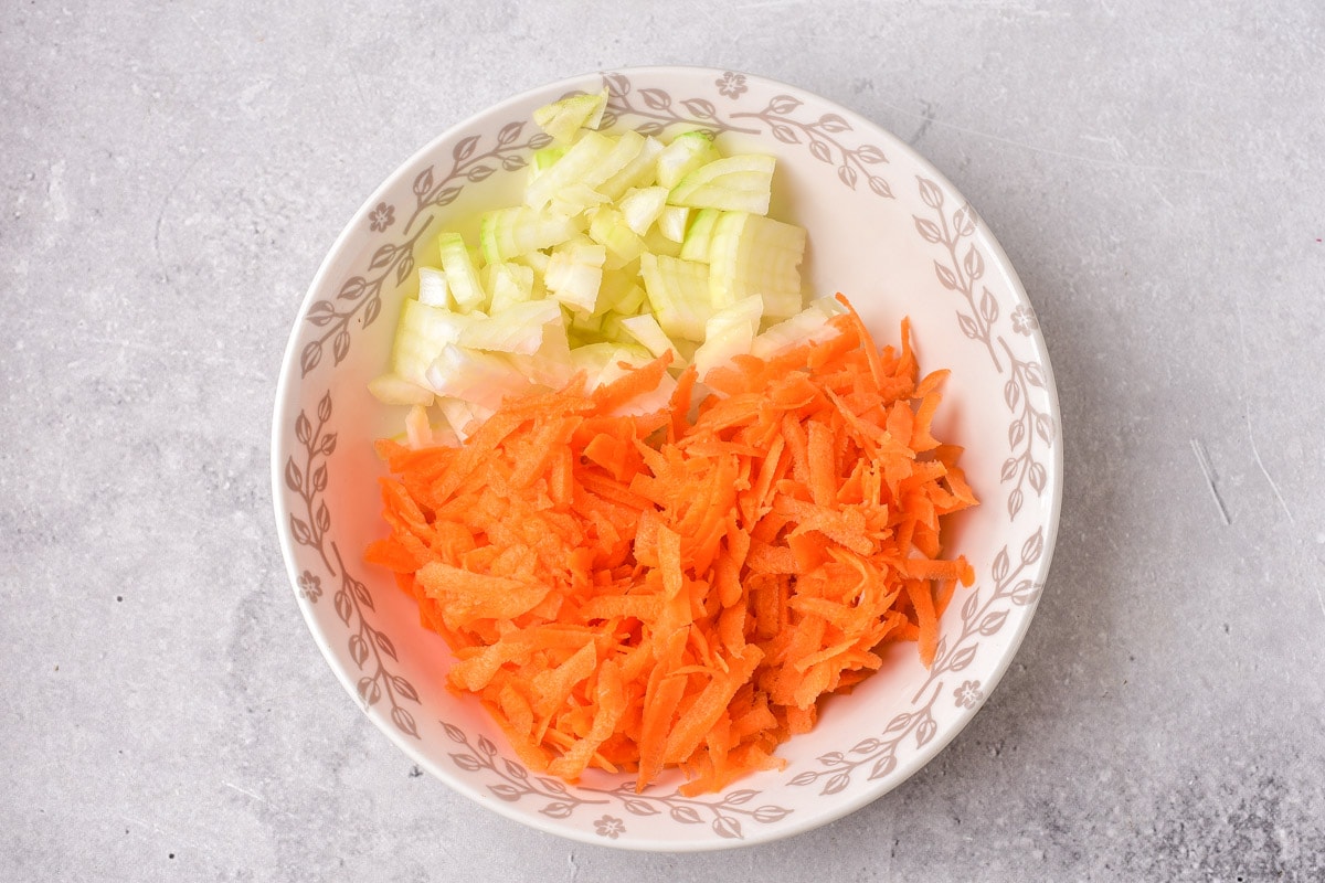 diced onions and grated carrots in bowl on counter top.