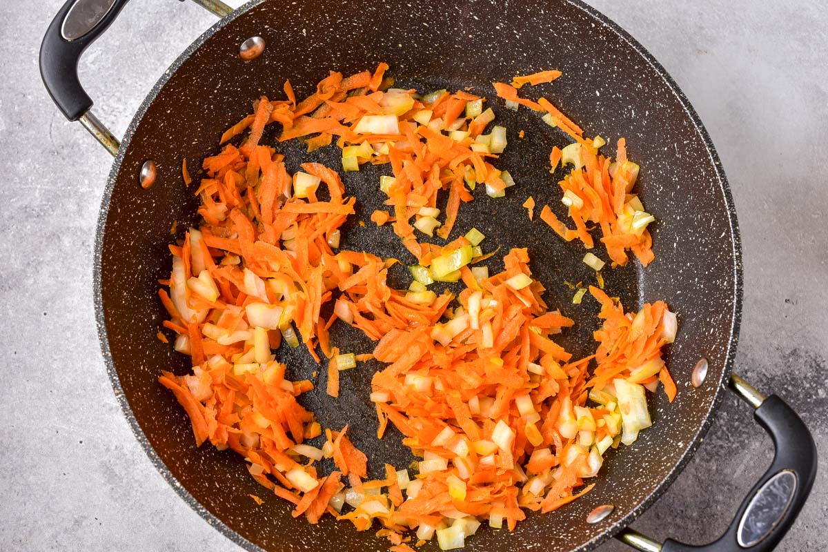 carrots and onions frying in black pan on stove top.