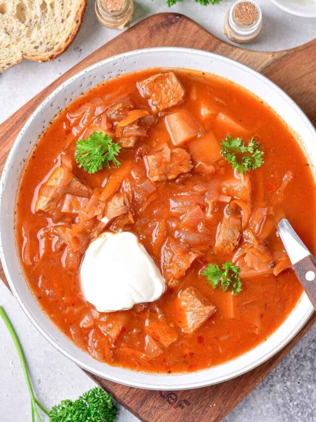 red borscht soup in bowl with parsley and sour cream on top.