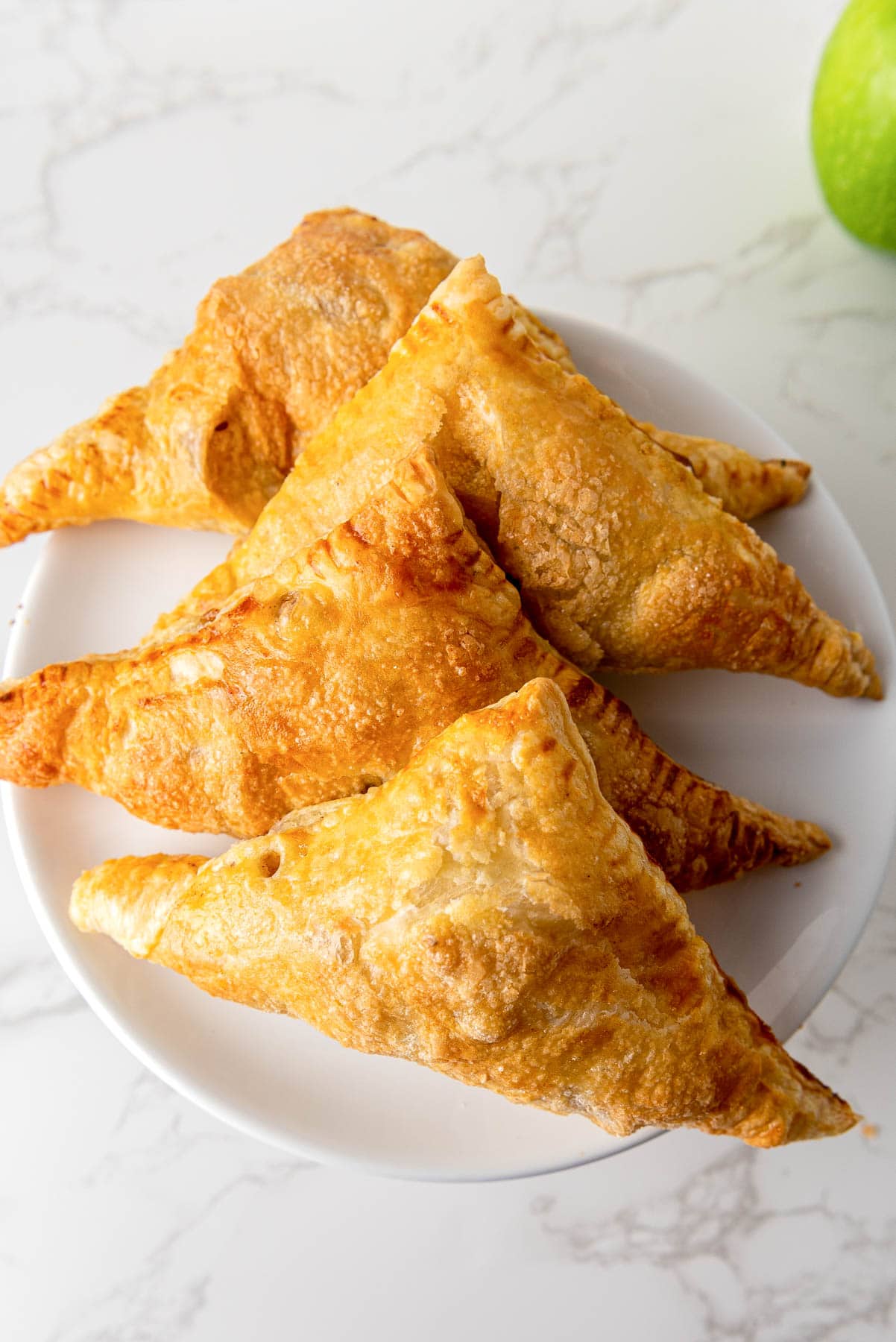 dutch apple turnovers on plate sitting on white counter top with green apple beside.