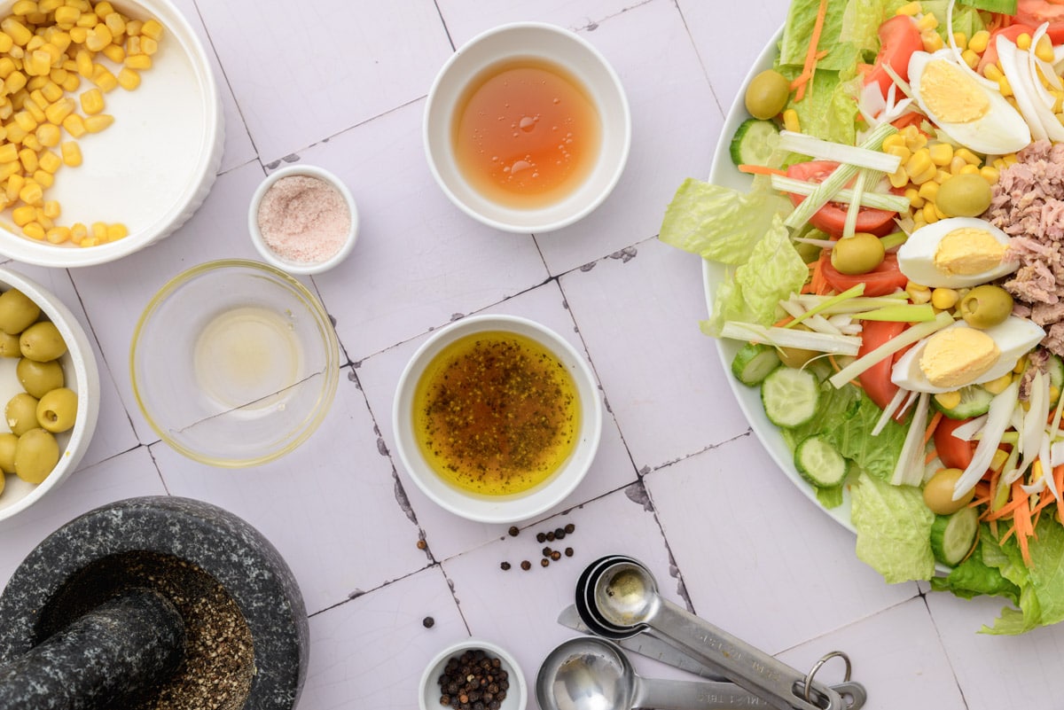 small bowls with ingredients for salad dressing like oil and vinegar on white counter top.