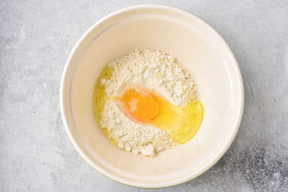 flour and egg in white mixing bowl on counter top.