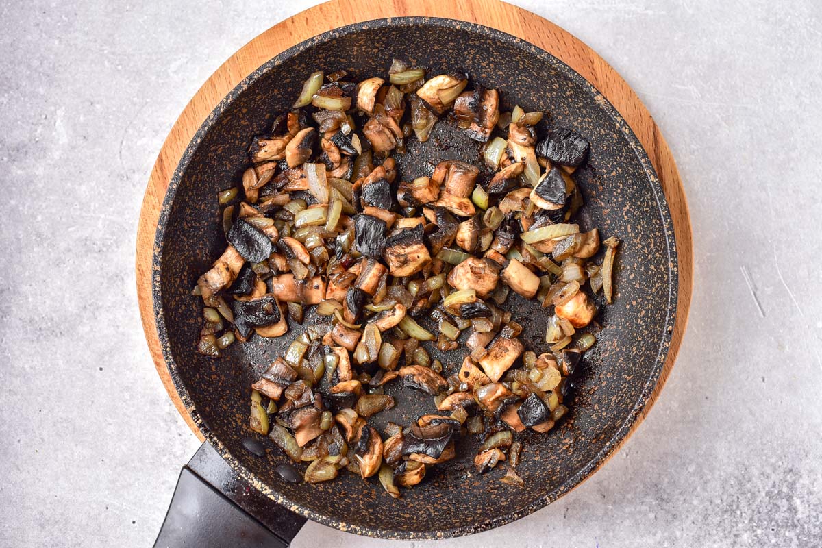 fried mushrooms and onions in black pan with grey counter around.