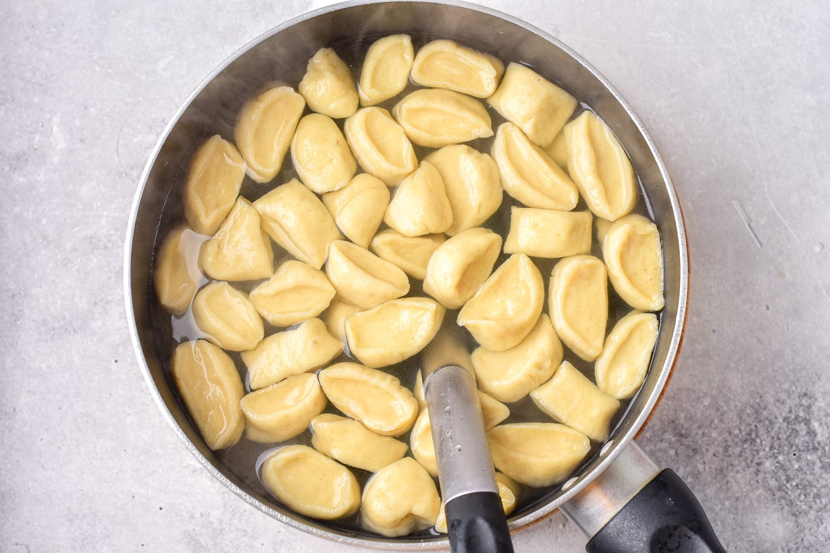 galushki dumplings in boiling water in silver pot with spoon inside.