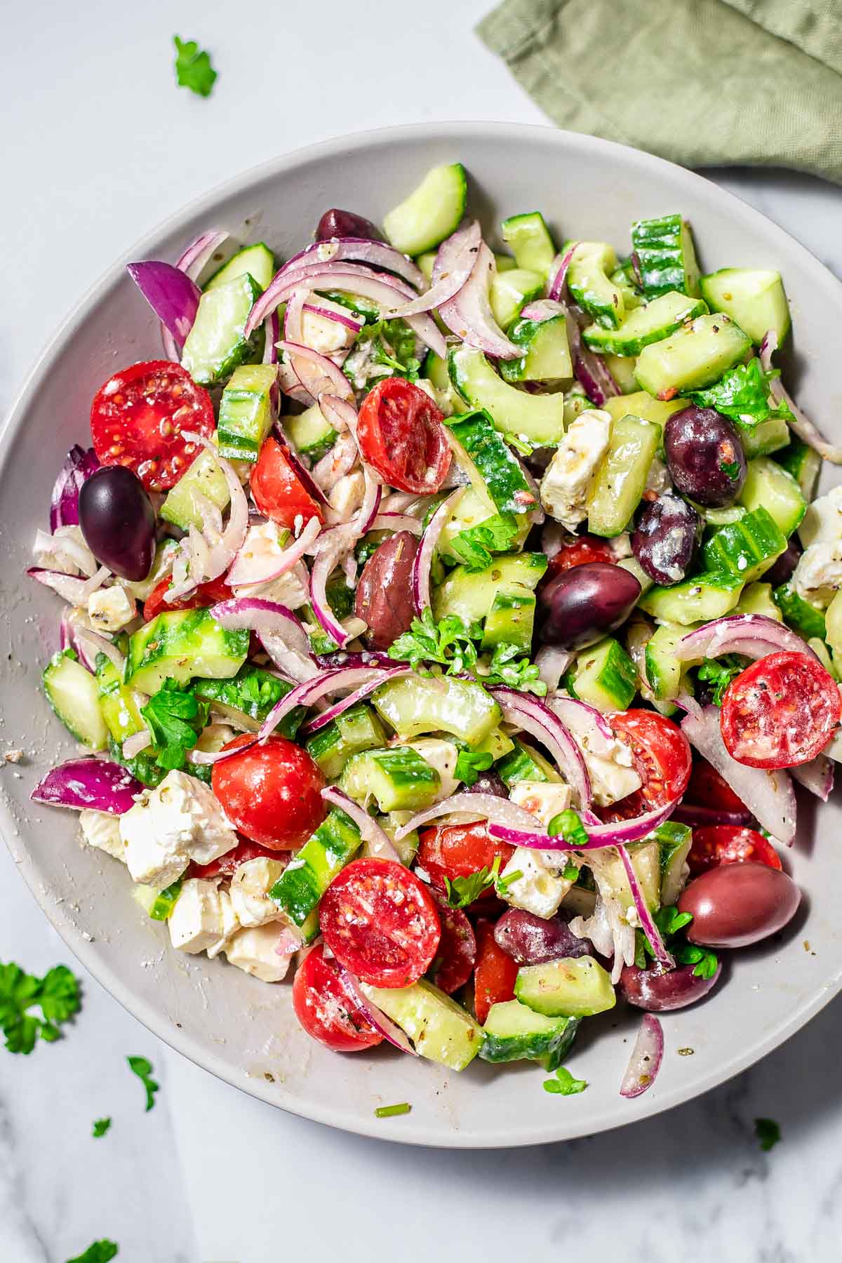 colorful greek salad on plate with dressing sitting on counter with parsley around.