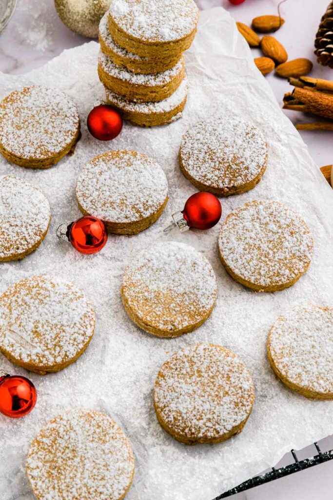 round spanish polvorones cookies on parchment paper with stack of cookies behind and red christmas bulbs beside.