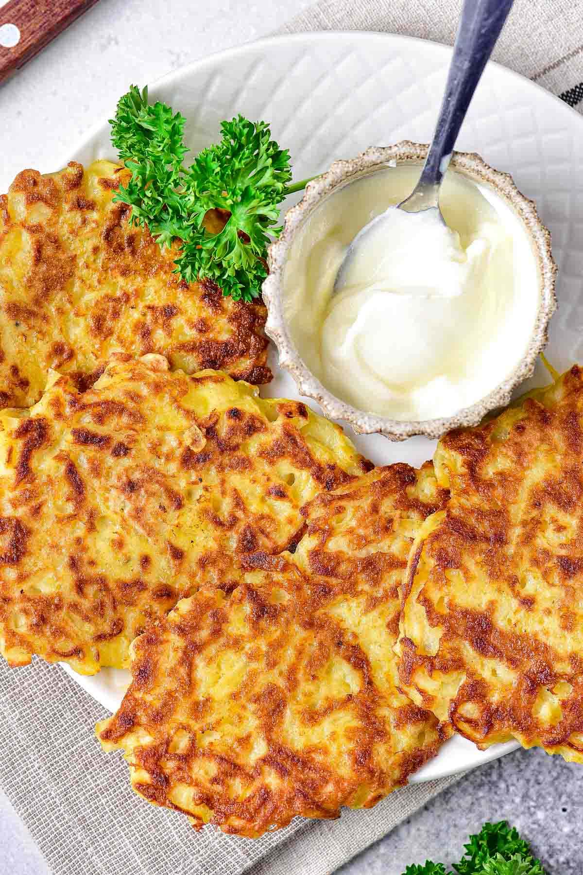 crispy potato pancakes on plate with spoon in sour cream and parsley beside.