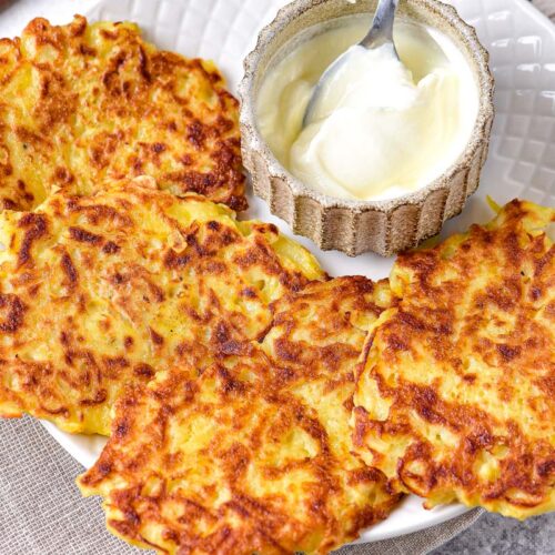 potato pancakes on plate with bowl of sour cream beside.